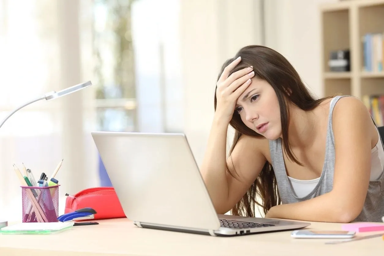 A woman sitting at her desk looking at the laptop.