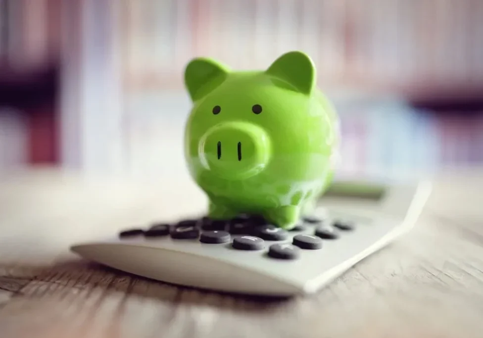 A green piggy bank sitting on top of a calculator.